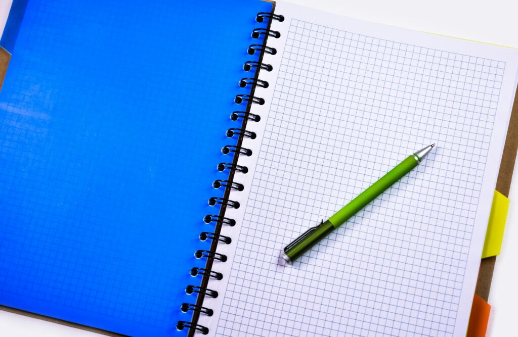 Open graphing notebook with a green pen on a white desk surface.